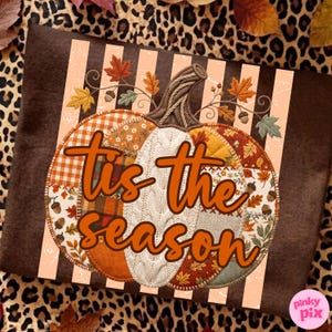 May include: A brown t-shirt featuring a graphic of a pumpkin made of various autumn-themed fabric patterns, including plaid, floral, and cable knit. The text 'tis the season' is printed in orange script over the pumpkin, surrounded by leaves.