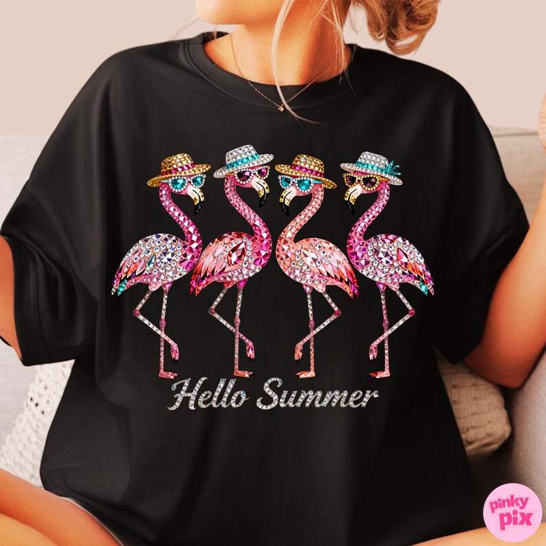 May include: Black t-shirt featuring four pink flamingo illustrations adorned with hats and sunglasses. Each flamingo is embellished with sparkling details. The phrase "Hello Summer" is written in a cursive font below the flamingos.