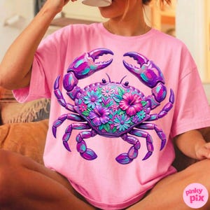 May include: Pink t-shirt featuring a vibrant crab design. The crab is adorned with purple, teal, and pink floral accents. The shirt is a solid pink color, and the crab graphic is centered on the front.