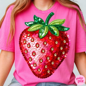 K&ouml;nnte beinhalten: Ein pinkfarbenes T-Shirt mit einem gro&szlig;en, paillettenbesetzten Erdbeermotiv. Die Erdbeere ist rot mit goldenen Akzenten und gr&uuml;nen Paillettenbl&auml;ttern. Das Shirt hat kurze &Auml;rmel und einen Rundhalsausschnitt.