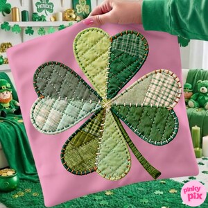 Può includere: Un cuscino rosa con un grande design a quadrifoglio trapuntato. Il quadrifoglio è realizzato con vari tessuti verdi con diversi motivi e trame. Il quadrifoglio è cucito con filo bianco. Il cuscino è tenuto da una persona.