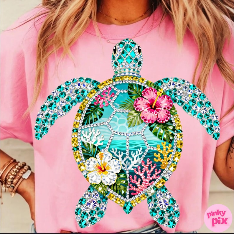 May include: Pink t-shirt featuring a bejeweled sea turtle design. The turtle has turquoise flippers and head, a yellow and white shell, and a central image of a tropical scene with flowers and coral.