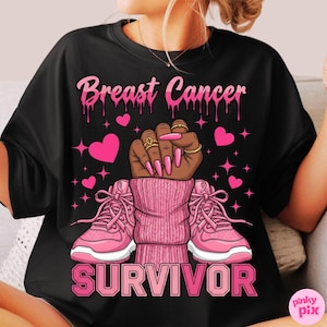 May include: Black t-shirt with a pink graphic design. The design includes the words "Breast Cancer Survivor" with a raised fist, pink hearts, and pink sneakers. The fist has gold rings and long pink nails.