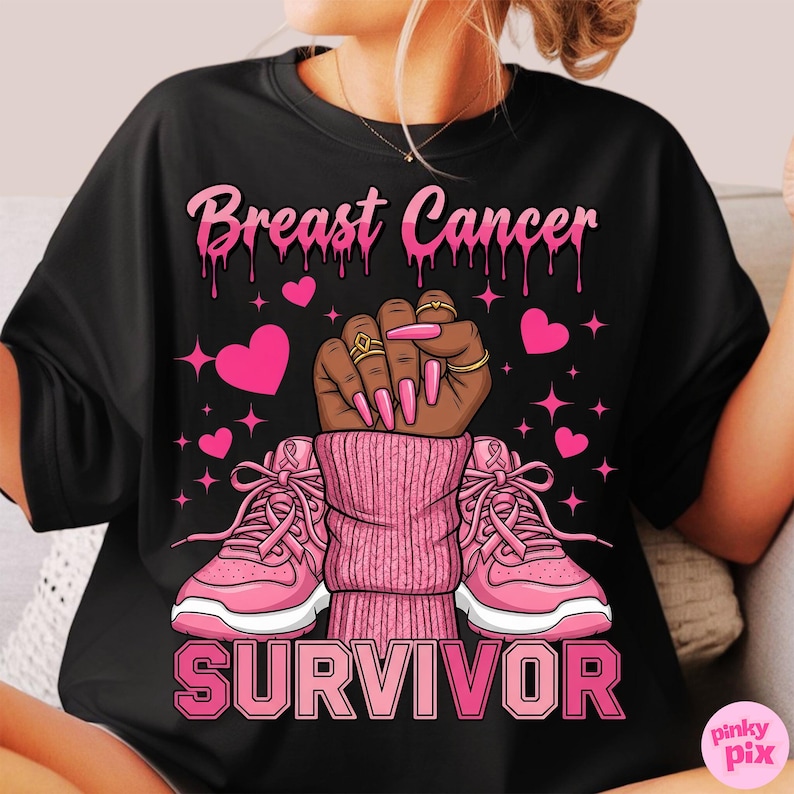 May include: Black t-shirt with a pink graphic design. The design includes the words "Breast Cancer Survivor" with a raised fist, pink hearts, and pink sneakers. The fist has gold rings and long pink nails.