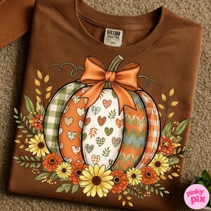 May include: Brown crew neck sweatshirt featuring a colorful pumpkin design. The pumpkin has sections with plaid, hearts, and chevron patterns, topped with an orange bow. The design is surrounded by fall flowers and foliage, perfect for autumn.