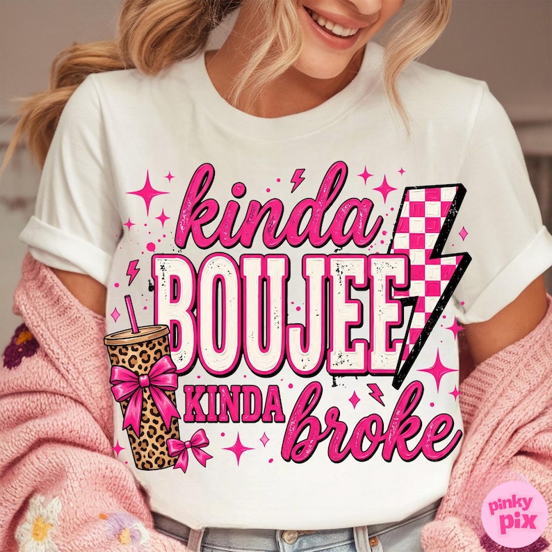 May include: A white short-sleeve t-shirt featuring a graphic design with the text "kinda BOUJEE kinda broke" in pink and black. The design includes a leopard print tumbler with a pink bow and a pink and white checkered lightning bolt icon.