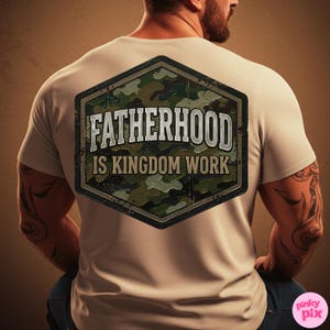 Pode incluir: Camiseta bege com o texto "FATHERHOOD IS KINGDOM WORK" em um design desgastado de estilo militar. O gr&aacute;fico &eacute; um hex&aacute;gono com um padr&atilde;o de camuflagem. A camiseta est&aacute; sendo usada.