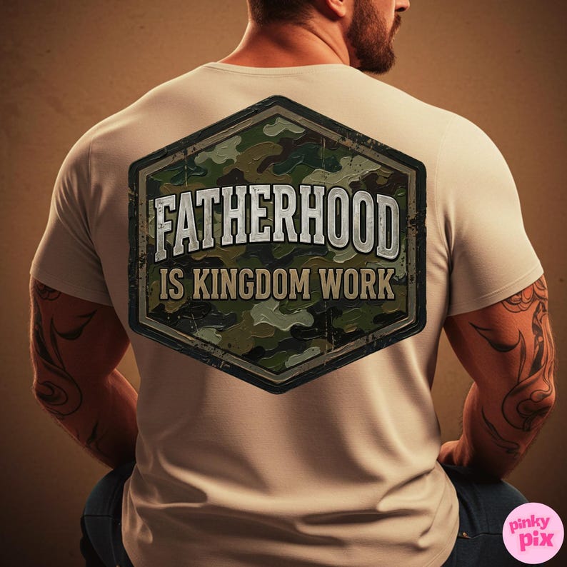 Pode incluir: Camiseta bege com o texto "FATHERHOOD IS KINGDOM WORK" em um design desgastado de estilo militar. O gr&aacute;fico &eacute; um hex&aacute;gono com um padr&atilde;o de camuflagem. A camiseta est&aacute; sendo usada.