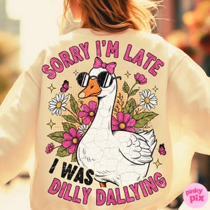 K&ouml;nnte beinhalten: Cremefarbenes Sweatshirt mit einer Grafik einer Gans mit Sonnenbrille und rosa Schleife. Der Text lautet "SORRY I'M LATE I WAS DILLY DALLYING" in Rosa. Das Design umfasst Blumen und Schmetterlinge.