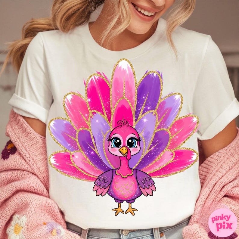 May include: White t-shirt featuring a cartoon turkey with a vibrant pink, purple, and gold feather design. The turkey has large blue eyes and is centered on the shirt. The text "pinky pix" is in the lower right corner.