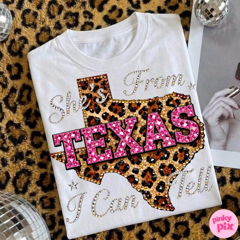 May include: White t-shirt with a leopard print Texas outline and the text "TEXAS" in pink rhinestones. The shirt also features the phrases "She's From" and "I Can Tell" in rhinestone lettering.