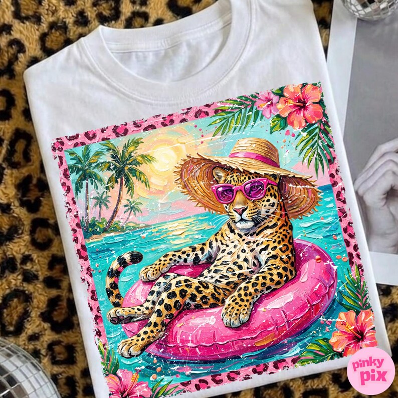 May include: White t-shirt with a leopard design. The leopard is wearing sunglasses and a straw hat, relaxing on a pink inflatable ring in the sea. The design includes palm trees, flowers, and a pink leopard print border. The text "pinky pix" is visible.