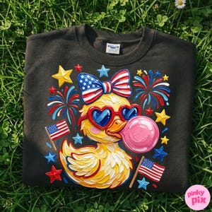 May include: Black sweatshirt featuring a yellow duck wearing heart-shaped sunglasses and a bow with an American flag design. The duck is blowing a pink bubble and surrounded by fireworks, stars, and American flags.