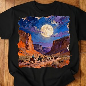 May include: Black t-shirt featuring a vibrant painting of cowboys riding horses through a canyon under a full moon. The artwork showcases a night scene with a blue sky, purple clouds, and orange canyon walls. The design is reminiscent of a Western theme.