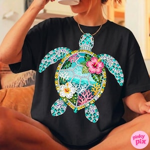 May include: Black t-shirt featuring a detailed, colorful sea turtle design. The turtle's shell is adorned with turquoise and clear gemstones, surrounding a tropical scene with flowers and coral. The design includes pink, white, and yellow flowers.