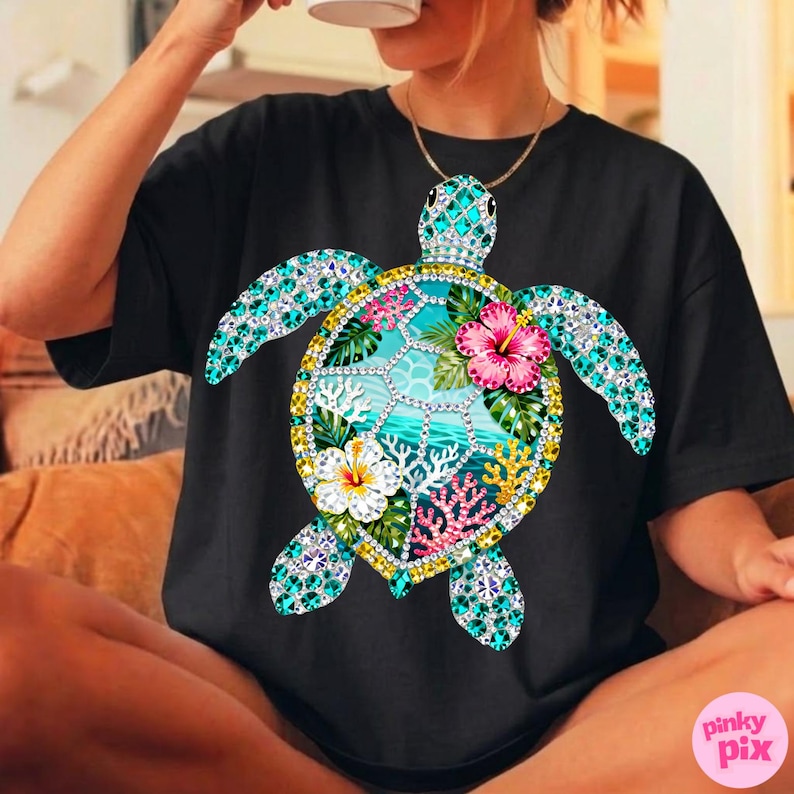 May include: Black t-shirt featuring a detailed, colorful sea turtle design. The turtle's shell is adorned with turquoise and clear gemstones, surrounding a tropical scene with flowers and coral. The design includes pink, white, and yellow flowers.