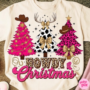 May include: A cream-colored t-shirt featuring three Christmas trees with cowboy hats, antlers, and bows. The trees are pink, black and white cow print, and pink leopard print. The text "HOWDY Christmas" is in a leopard print font.