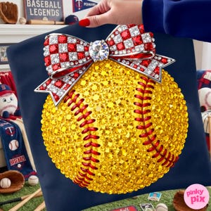 May include: A decorative softball cushion with a yellow crystal-covered surface and red stitching. A red, white, and silver bow with a large crystal centrepiece adorns the top. The cushion is set against a navy blue background.