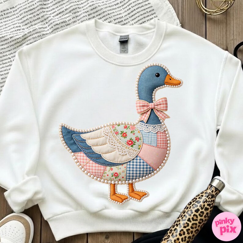K&ouml;nnte beinhalten: Wei&szlig;es Sweatshirt mit einem gro&szlig;en, applizierten G&auml;nsemotiv. Die Gans hat einen blauen Kopf, einen orangefarbenen Schnabel und F&uuml;&szlig;e sowie eine rosa Schleife. Ihr K&ouml;rper ist ein Patchwork aus floralen, Vichy- und unifarbenen Stoffen, umrandet mit Perlen. Ein charmantes und skurriles Design.