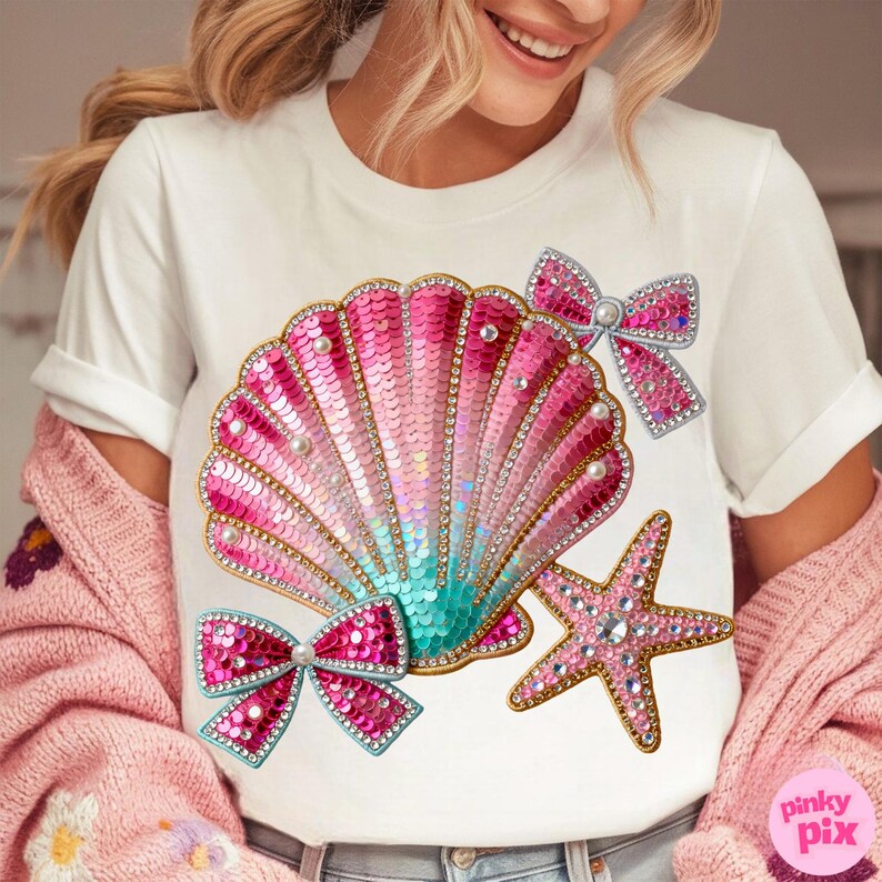 May include: White t-shirt featuring a sequined seashell design in shades of pink and teal, adorned with pearls and rhinestones. Two pink sequined bows and a starfish complete the design. The text "pinky pix" is in the bottom right corner.