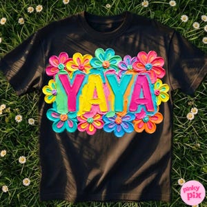May include: Black t-shirt with the word "YAYA" in bright pink, yellow, and teal, surrounded by colorful, textured flowers. The flowers have a 3D effect, with shades of pink, yellow, blue, and orange.