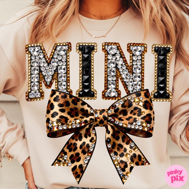 Pu&ograve; includere: Una felpa beige con la scritta "MINI" in lettere gioiello. La "M" e la "N" sono decorate con strass trasparenti, mentre le "I" sono nere. Un grande fiocco leopardato con dettagli di strass e oro &egrave; centrato sotto la scritta.
