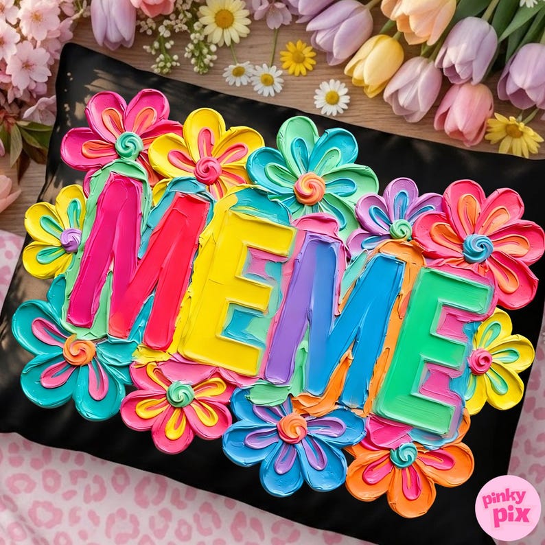 May include: Black pillow with the word "MEME" in colorful, textured letters, surrounded by vibrant, 3D-effect flowers in shades of pink, yellow, blue, and orange. The pillow is a decorative item.