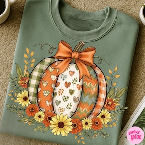 May include: Sage green sweatshirt featuring a colorful pumpkin design. The pumpkin is decorated with plaid, hearts, and knit patterns, topped with an orange bow. Sunflowers and fall foliage surround the pumpkin, creating a seasonal theme.