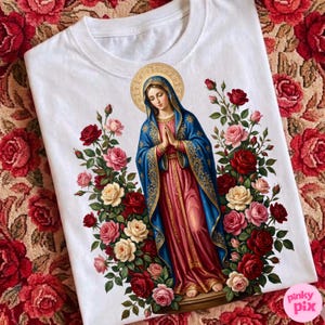 May include: White t-shirt featuring a religious illustration of a woman in a blue and red robe, surrounded by red, pink, and cream roses. The design includes a gold halo and intricate details.