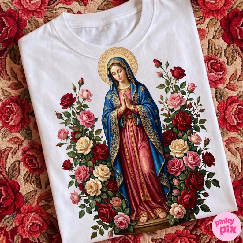 May include: White t-shirt featuring a religious illustration of a woman in a blue and red robe, surrounded by red, pink, and cream roses. The design includes a gold halo and intricate details.