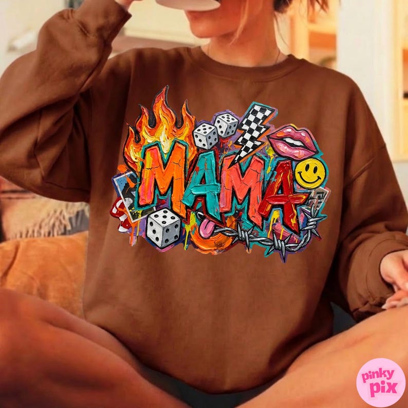 May include: Brown sweatshirt with a colorful graphic design that says "MAMA". The design includes flames, dice, a lightning bolt, lips, a smiley face, and barbed wire. The sweatshirt is a solid brown color.
