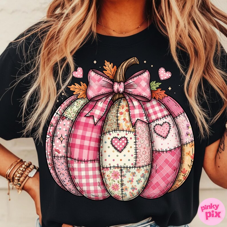 May include: Black t-shirt featuring a pink patchwork pumpkin design. The pumpkin has a pink bow, heart accents, and various patterned sections, including gingham and floral prints. The design is a fall or autumn theme.