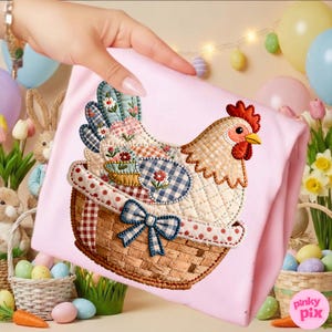 May include: A pink fabric item with an embroidered chicken design. The chicken is in a basket with a blue bow. The chicken has a patchwork design with floral and gingham patterns. Easter-themed decor is in the background.