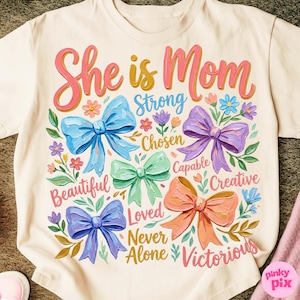 K&ouml;nnte beinhalten: Cremefarbenes T-Shirt mit dem Schriftzug "She is Mom" in rosa und gelb. Das Design umfasst bunte Schleifen, Blumen und inspirierende W&ouml;rter wie "Strong", "Beautiful" und "Victorious".