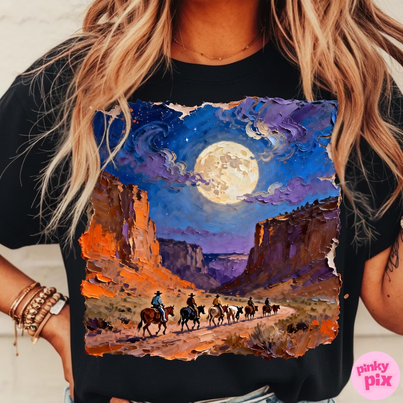 May include: Black t-shirt featuring a vibrant, impressionistic painting of a desert canyon scene under a full moon. Cowboys on horseback ride along a path, with the night sky filled with stars and clouds. The artwork has a textured, painted look.
