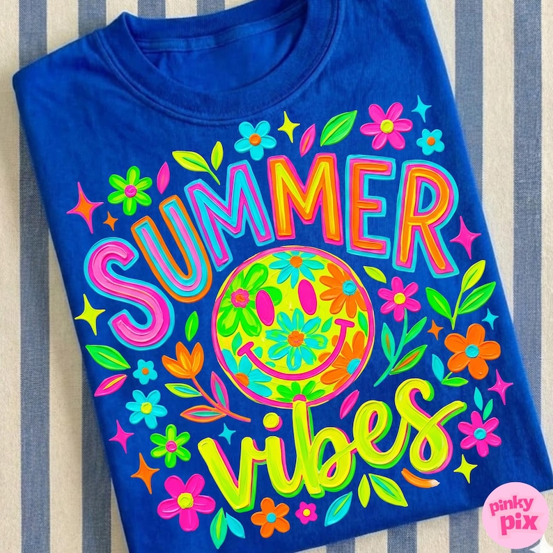 May include: A royal blue t-shirt with a colorful graphic design. The design features the words "SUMMER VIBES" in bright, outlined letters, a smiley face made of flowers, and various floral accents. The shirt is a casual summer style.