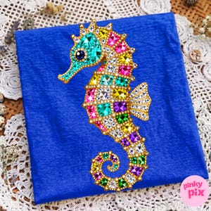 May include: A colorful seahorse design with a gold outline and encrusted with various colored gems. The seahorse is set against a blue background. The seahorse's body is adorned with gems in shades of turquoise, pink, yellow, and purple.