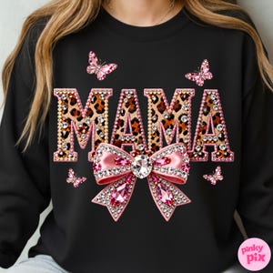 May include: Black sweatshirt with the word "MAMA" in leopard print letters outlined with rhinestones. A pink bow with a large crystal center and pink rhinestones is below the word. Pink butterflies are scattered around the design.