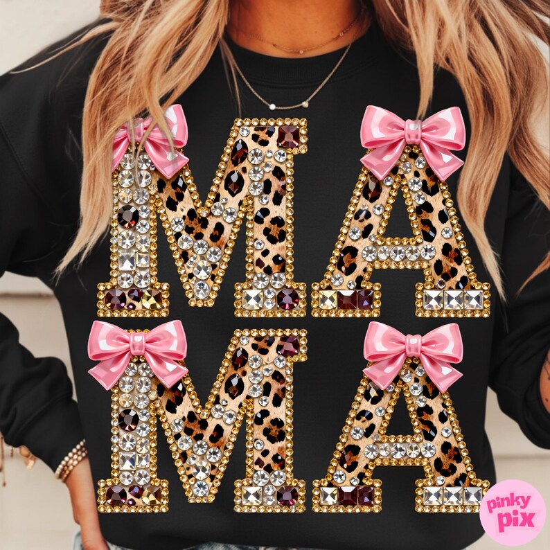 May include: Black sweatshirt featuring the word "MAMA" in large, embellished letters. The letters have a gold outline and leopard print filling. Pink bows are attached to the top of each letter.