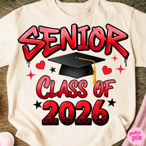 Puede incluir: Camiseta color crema con un diseño gráfico rojo y negro. El diseño incluye la palabra "SENIOR" en estilo grafiti, un birrete y el texto "CLASS OF 2026". También se incluyen corazones y estrellas.