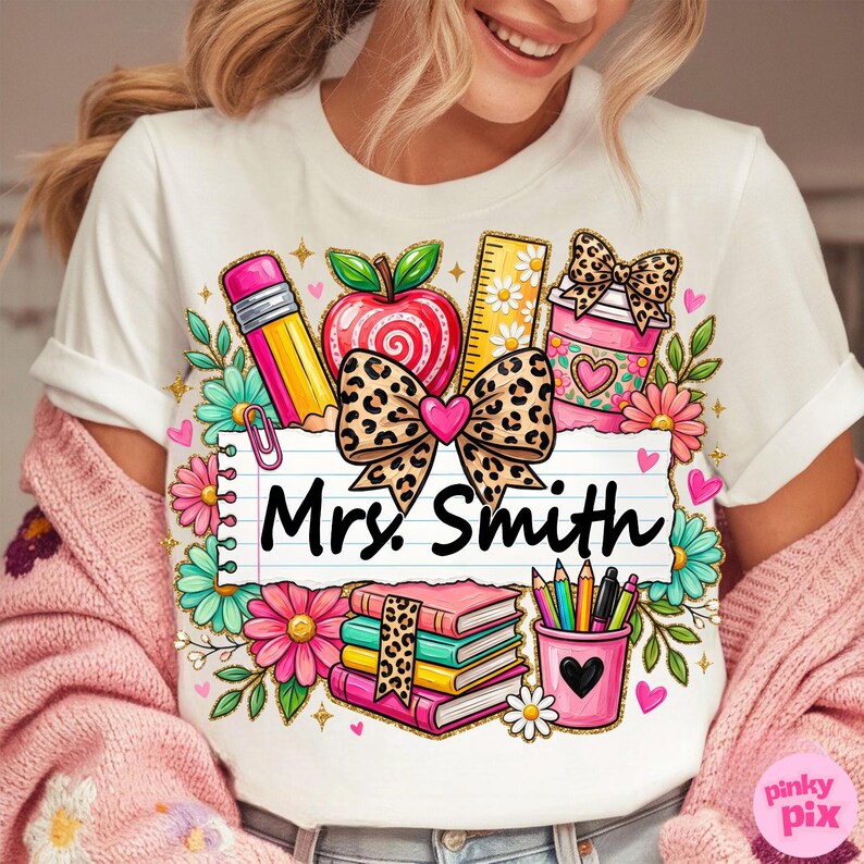 May include: White t-shirt with a colorful teacher-themed graphic. The design includes a pencil, apple, ruler, coffee cup, books, and pencils. A leopard print bow and the name "Mrs. Smith" are also featured.