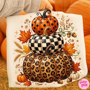 May include: A square fabric panel featuring a stack of three pumpkins with distinct patterns: a top orange pumpkin with black polka dots, a middle pumpkin with a black and white checkerboard pattern, and a bottom pumpkin with a brown leopard print.