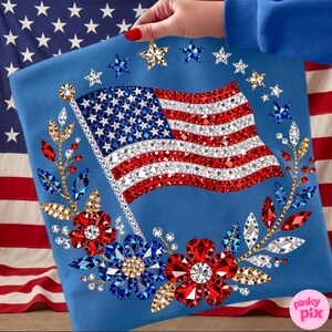 May include: A blue decorative item featuring a sparkling American flag design. The flag is embellished with red, white, and blue crystals. The design includes crystal stars and floral accents, creating a patriotic theme.