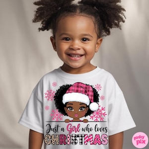 May include: White t-shirt featuring a graphic of a girl wearing a pink plaid Santa hat, surrounded by pink snowflakes. The text reads "Just a Girl who loves CHRISTMAS" in a mix of fonts and patterns. The shirt is for children.