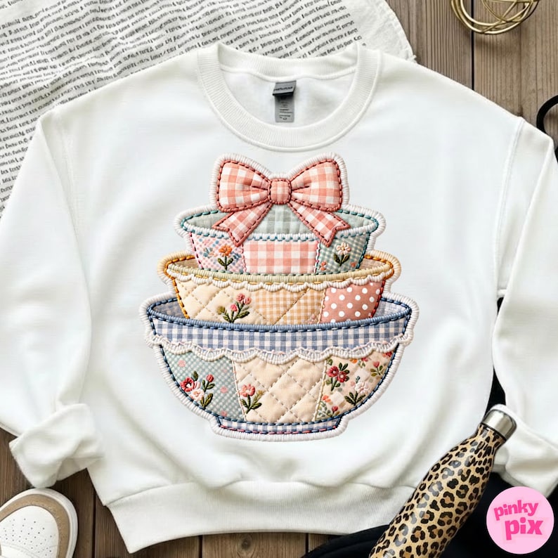 Puede incluir: Sudadera blanca con un dise&ntilde;o de cuencos apilados y un lazo. Los cuencos tienen un patr&oacute;n de patchwork con detalles florales y de cuadros en rosa, azul y amarillo. Un gr&aacute;fico encantador de inspiraci&oacute;n vintage.