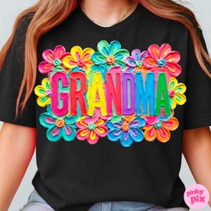 May include: Black t-shirt with the word "GRANDMA" in colorful, textured letters, surrounded by vibrant, multi-colored flowers. The flowers include shades of pink, yellow, blue, and orange.