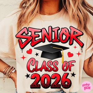 May include: Cream-colored t-shirt with the words "SENIOR CLASS OF 2026" in red, outlined in black, with a graduation cap graphic. The design includes hearts and stars.