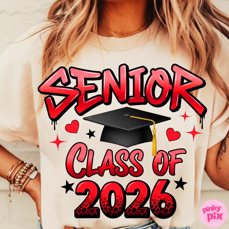 May include: Cream-colored t-shirt with the words "SENIOR CLASS OF 2026" in red, outlined in black, with a graduation cap graphic. The design includes hearts and stars.