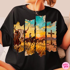 May include: Black t-shirt featuring a Western-themed graphic. The design includes a bull, a cowboy on horseback, and a cross, set against a sunset backdrop. The artwork has a textured, painted appearance, with a color palette of browns, oranges, and blues.