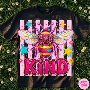 May include: Black t-shirt featuring a colorful illustration of a bee with a bow and the word "KIND" in pink. The bee has yellow and pink stripes, with blue, yellow, and pink stars around it. The background has pink and white stripes.